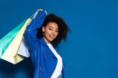 smiling african american woman with shopping bags on blue background