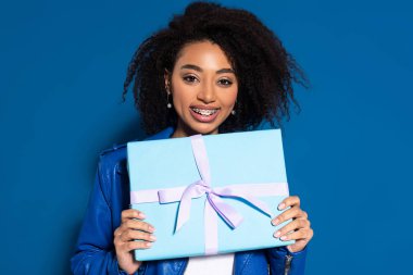 smiling african american woman holding present on blue background