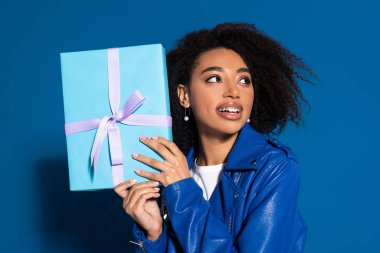 smiling african american woman holding present on blue background