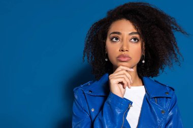 pensive african american woman looking away on blue background