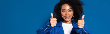 smiling african american woman showing thumbs up on blue background, panoramic shot clipart