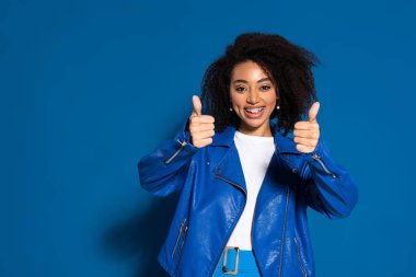 smiling african american woman showing thumbs up on blue background
