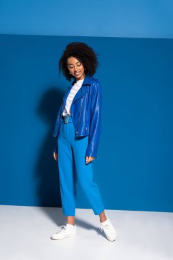 full length view of smiling african american woman on blue background
