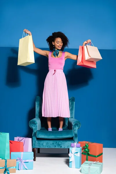 Sonriente Mujer Afroamericana Pie Sillón Terciopelo Con Bolsas Compras Cerca — Foto de Stock