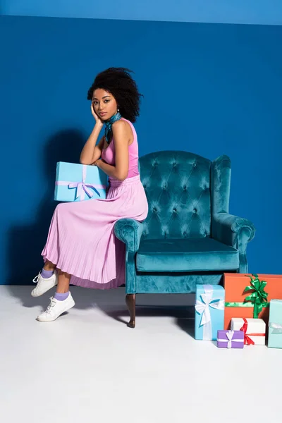 African American Woman Sitting Velour Armchair Gift Boxes Blue Background — Stock Photo, Image