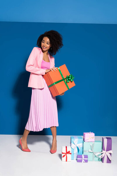 элегантная улыбающаяся африканская американка рядом с подарками на синем фоне
