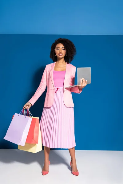 Κομψή Αφροαμερικανίδα Επιχειρηματίας Τσάντες Ψώνια Χρησιμοποιώντας Φορητό Υπολογιστή Μπλε Φόντο — Φωτογραφία Αρχείου