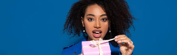 Shocked African American Woman Opening Gift Isolated Blue Panoramic Shot — Stok fotoğraf