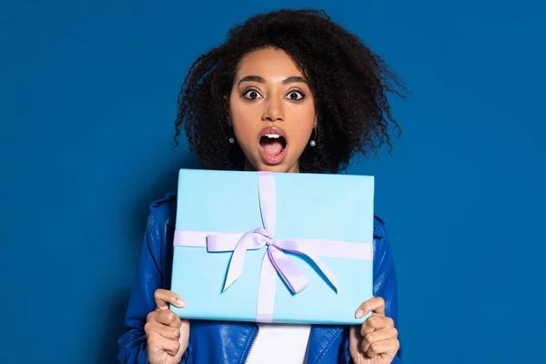 Shocked African American Woman Holding Present Blue Background — Stok fotoğraf