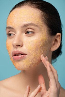 attractive girl applying yellow sugar scrub on face, isolated on blue clipart