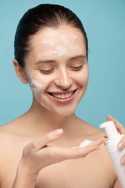 Gülümseyen kız şişeden köpük temizliyor, mavi renkte izole edilmiş.