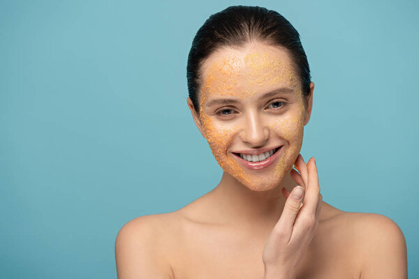 красивая веселая девушка, нанося желтый сахарный скраб на лицо, изолированные на синий
