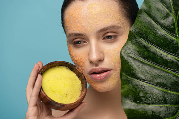 привлекательная девушка держит сахарный скраб в деревянной чаше, изолированный на синий с зеленым листом
