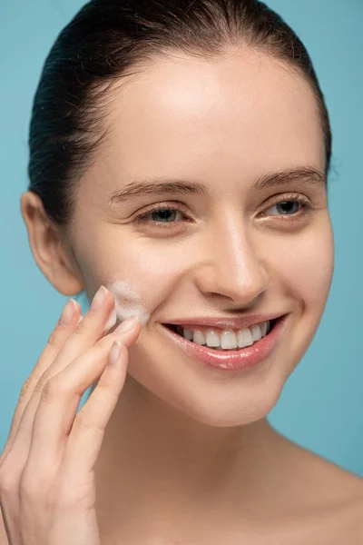 Sorrindo Jovem Mulher Aplicando Espuma Limpeza Rosto Isolado Azul — Fotografia de Stock