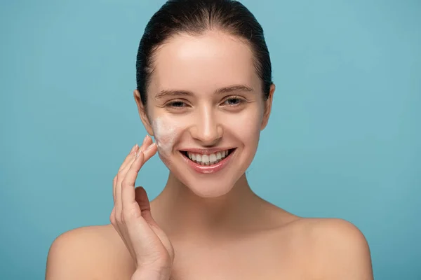 beautiful cheerful woman applying cleansing foam on face, isolated on blue