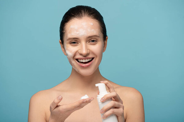 happy girl applying cleansing foam from bottle, isolated on blue