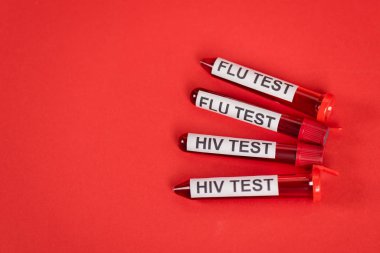 Kırmızı üzerinde HIV testi ve grip testi olan test tüplerinin üst görünümü 
