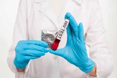 Lateks eldivenli bir bilim adamının elinde HIV testi harfleri ve beyaz üzerinde izole edilmiş prezervatif olan bir örnek vardı. 