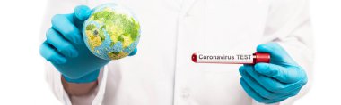 Küreyi tutan bilim adamının panoramik görüntüsü ve beyaz üzerine izole edilmiş koronavirüs test harfleri. 