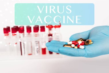 cropped view of scientist in latex glove holding pills near test tubes and virus vaccine lettering on white  clipart