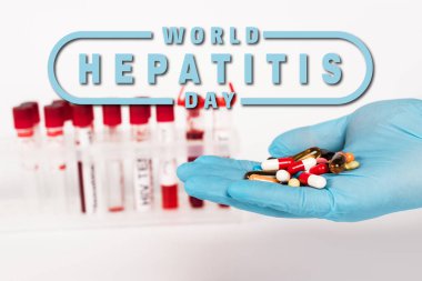 cropped view of scientist in latex glove holding pills near test tubes and world hepatitis day lettering on white  clipart