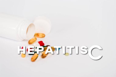 Renkli hapların yanında bir şişe ve beyazın üzerinde hepatit c harfleri var.