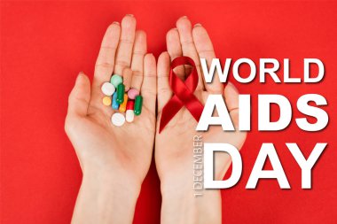 top view of woman holding red ribbon and pills near world aids day lettering on red  clipart