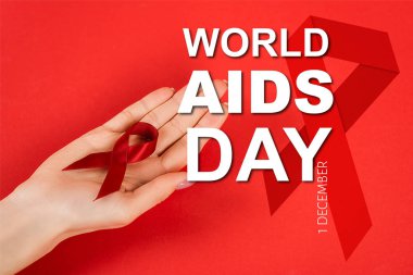 cropped view of woman holding red ribbon near world aids day lettering on red  clipart