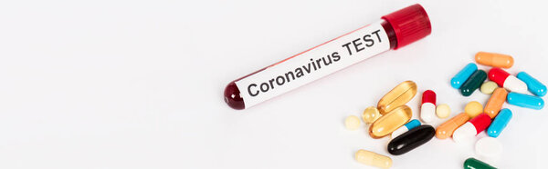 panoramic shot of colorful pills near sample with coronavirus test lettering isolated on white 