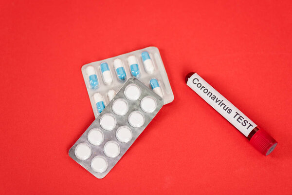top view of sample with coronavirus test lettering near pills in blister packs on red