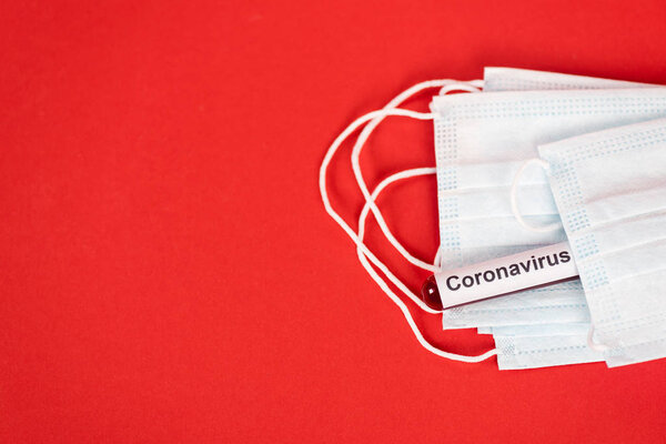 top view of sample with coronavirus lettering near protective medical masks on red 