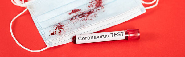panoramic shot of sample with coronavirus test lettering near medical mask with blood on red 