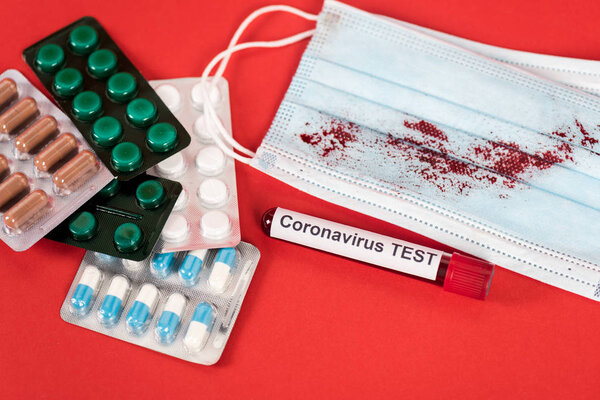 sample with coronavirus test lettering near pills and medical mask with blood on red 