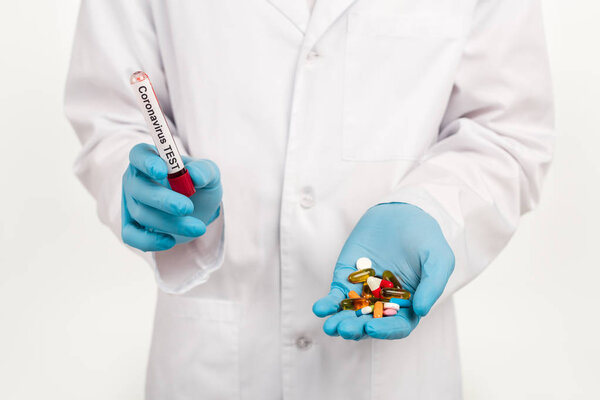 cropped view of scientist holding sample with coronavirus test lettering and pills isolated on white 