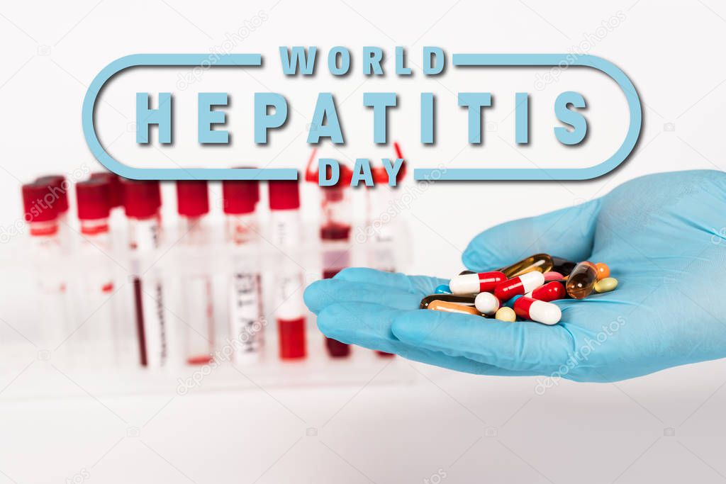 cropped view of scientist in latex glove holding pills near test tubes and world hepatitis day lettering on white 