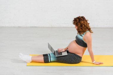Hamile kadının spor paspası olarak dizüstü bilgisayar kullanmasının yan görüntüsü