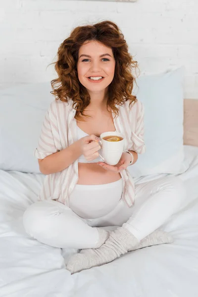 美しいです妊娠中の女性とともにお茶のカップでカメラでベッド — ストック写真