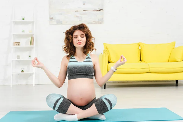 身披荷花的孕妇在客厅的健身垫上摆姿势 — 图库照片