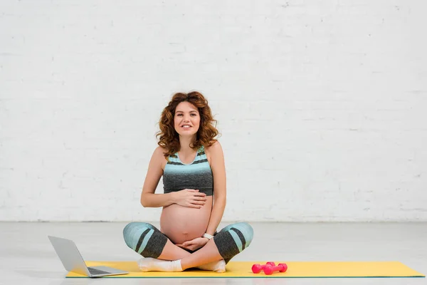 Mulher Grávida Sorrindo Para Câmera Tocar Barriga Perto Laptop Halteres — Fotografia de Stock