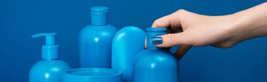 panoramic shot of woman holding bottle with shampoo on blue background clipart