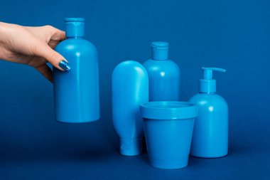 cropped view of woman holding bottle with shampoo on blue background clipart