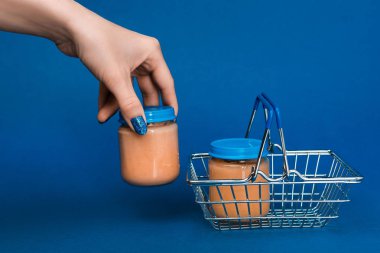 cropped view of woman putting in shopping basket jar with baby food on blue background  clipart