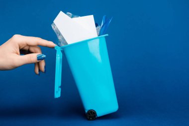 cropped view of woman touching toy trash can on blue background  clipart