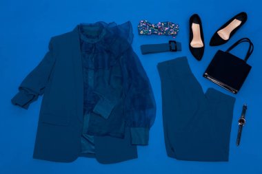 Bluz, ceket, pantolon, topuklar, kemer, çanta, kol saati mavi üzerine izole edilmiş.