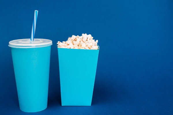 paper cup and popcorn on blue background with copy space 