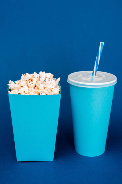 paper cup and popcorn on blue background with copy space 
