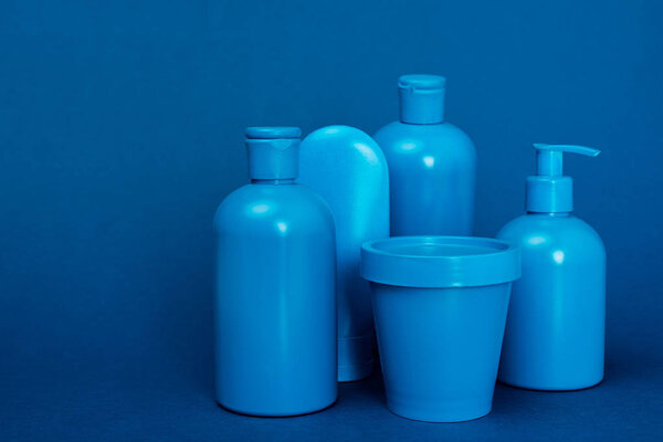 бутылки с кондиционером для волос, шампунь, гель для душа, жидкое мыло и ведро на синем фоне
