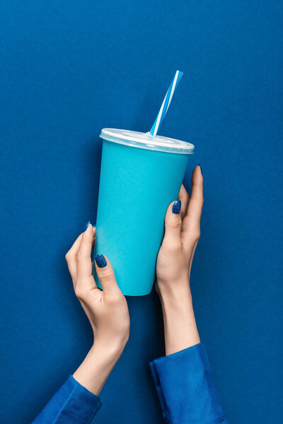 cropped view of woman holding paper cup on blue background 