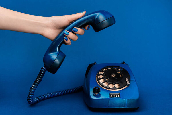 cropped view of woman holding handset on blue background 