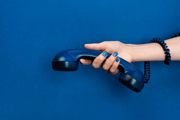 cropped view of woman holding handset on blue background 